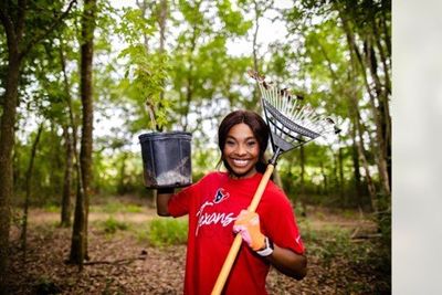 Houston Texans cheerleader holds up new tree and rake in Hermann Park Conservancy