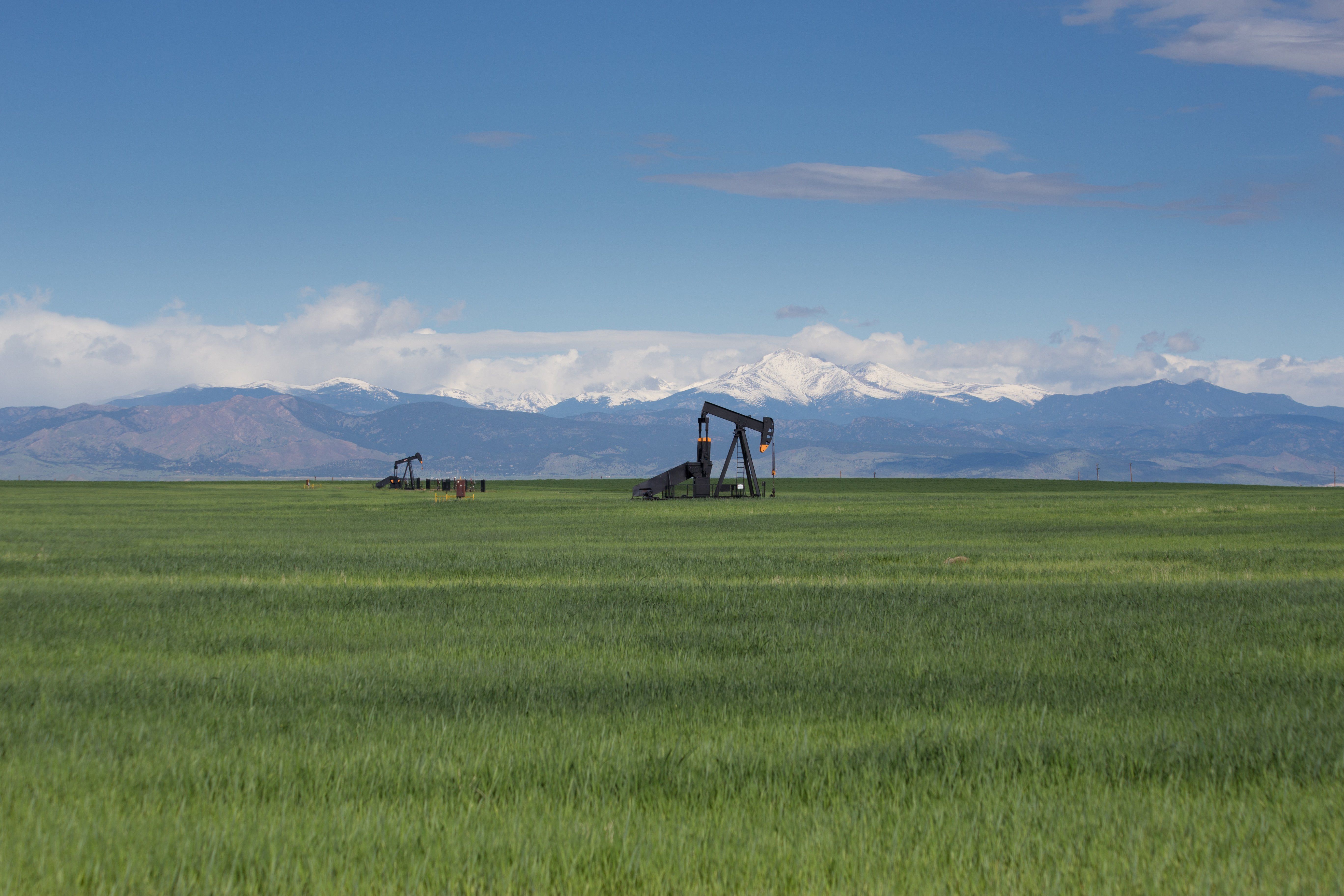 Pump jacks in green field with snow-covered Rocky Mountains and blue sky background