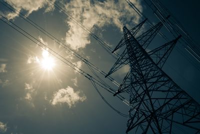 looking up at electric power pylon from below with bright sun radiating down